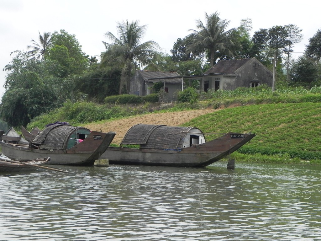 two boats docked on a river with some huts on the shore