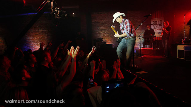 a man wearing a hat with his hands up in the air as he stands on stage