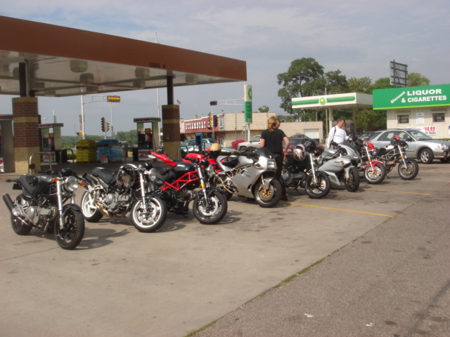 several motor bikes line up in a row by a gas station