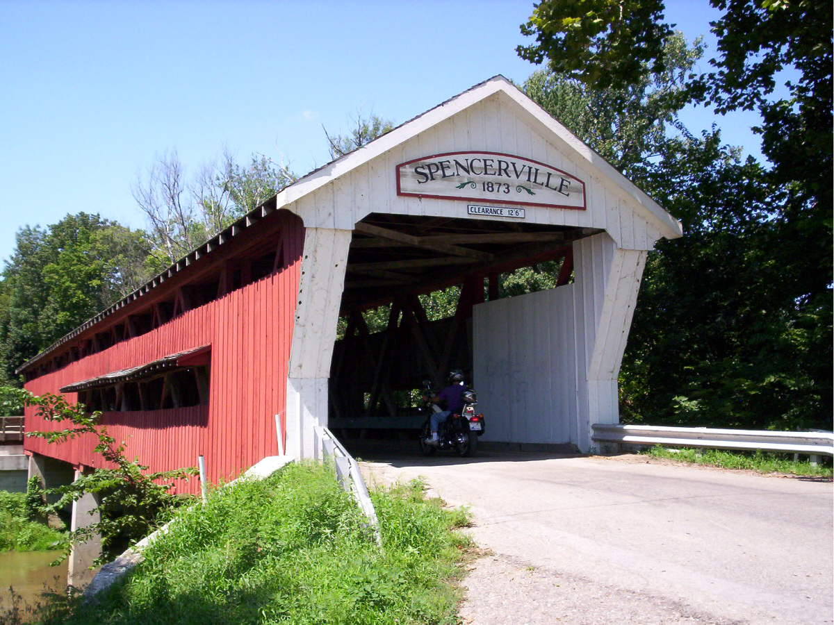 there is a biker riding down the road by a covered bridge