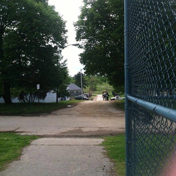 a fence is by the curb on a dirt road