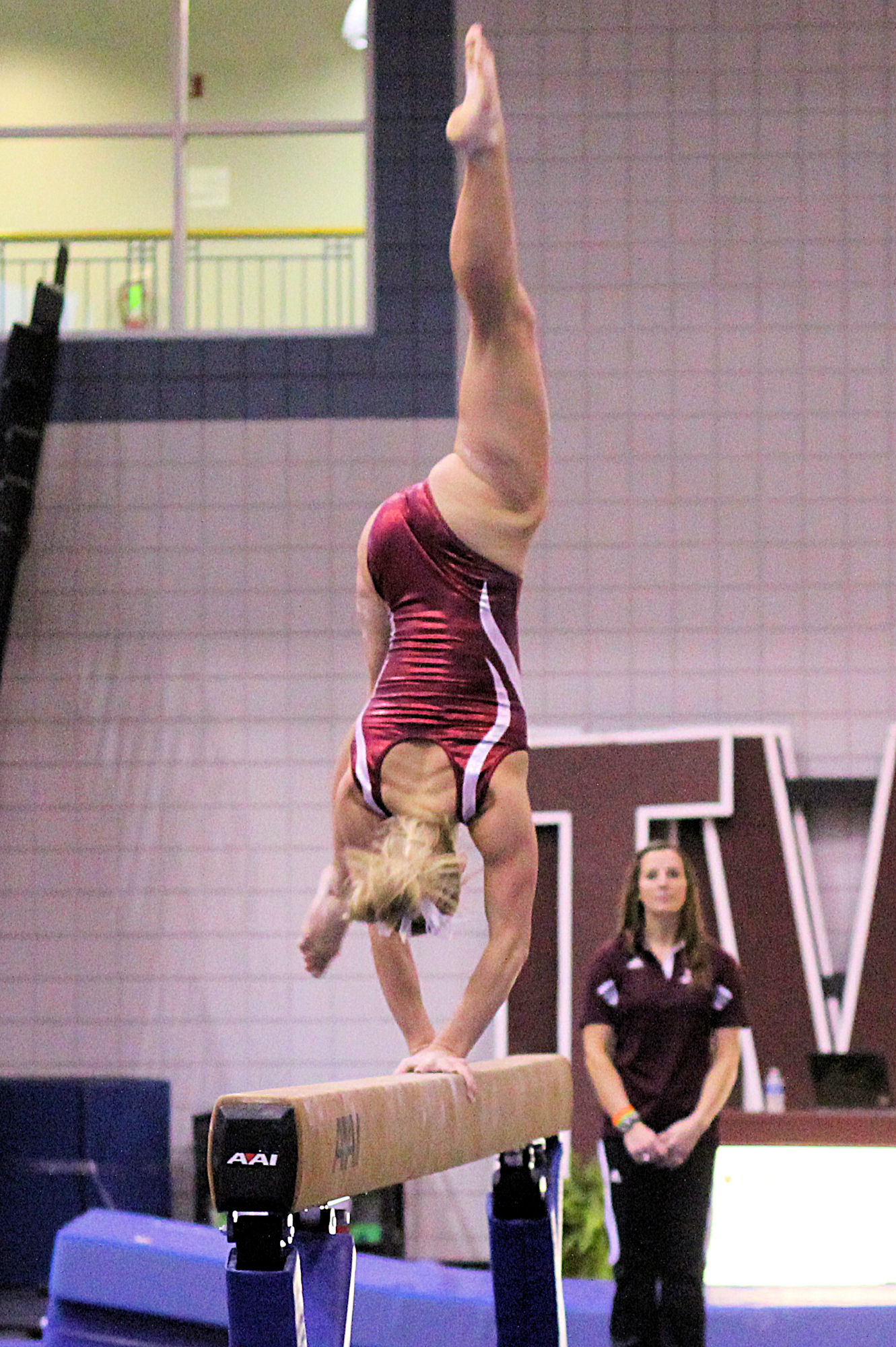 a young woman in a maroon and white leotard doing a splits exercise on the parallel bars