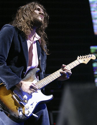 a man with long hair and a beard plays an electric guitar