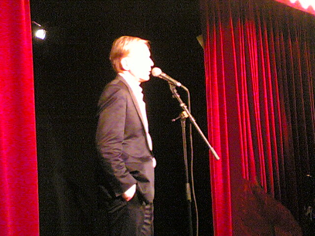 a man standing in front of a microphone with red curtains