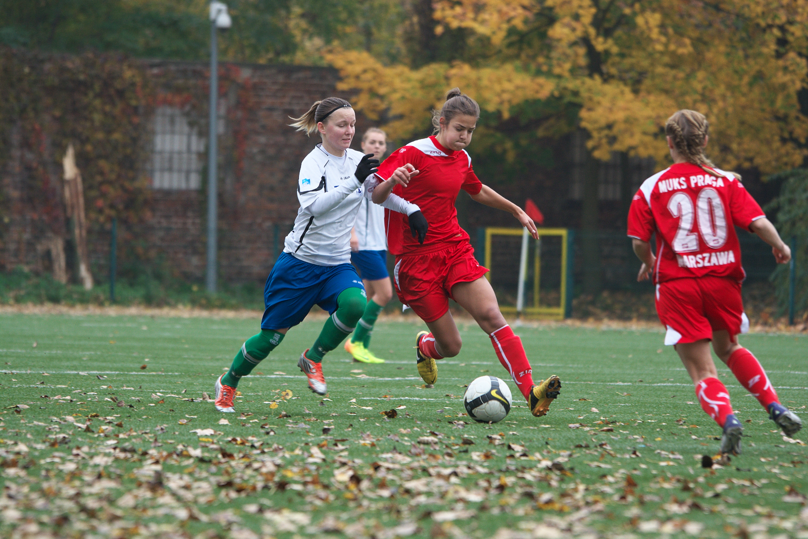 three female soccer players running after a soccer ball