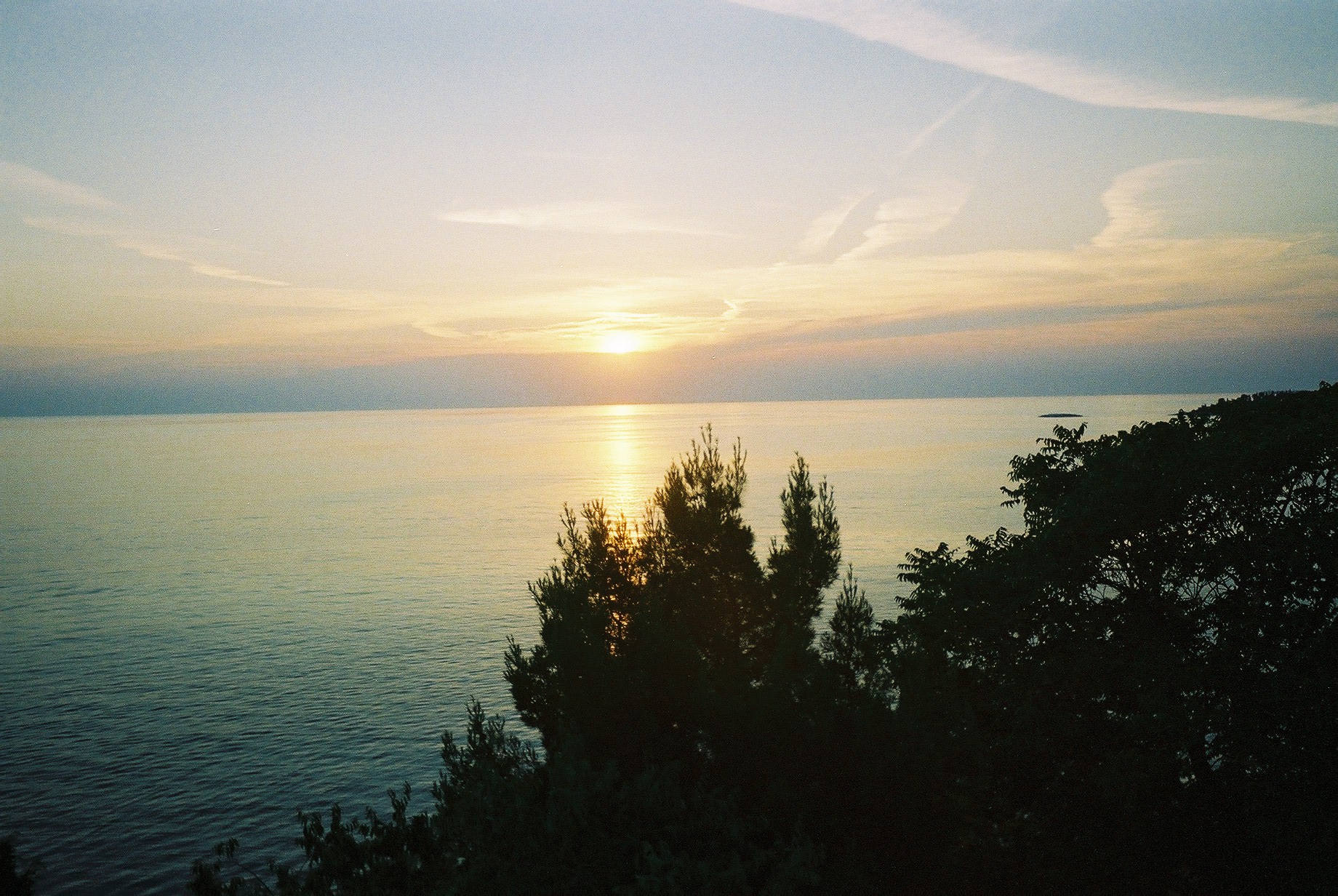 the sun peeking over the water with a forest in front