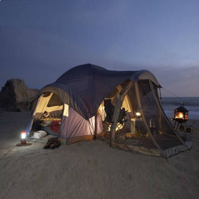 a tent on the sand with two campers setting up inside it