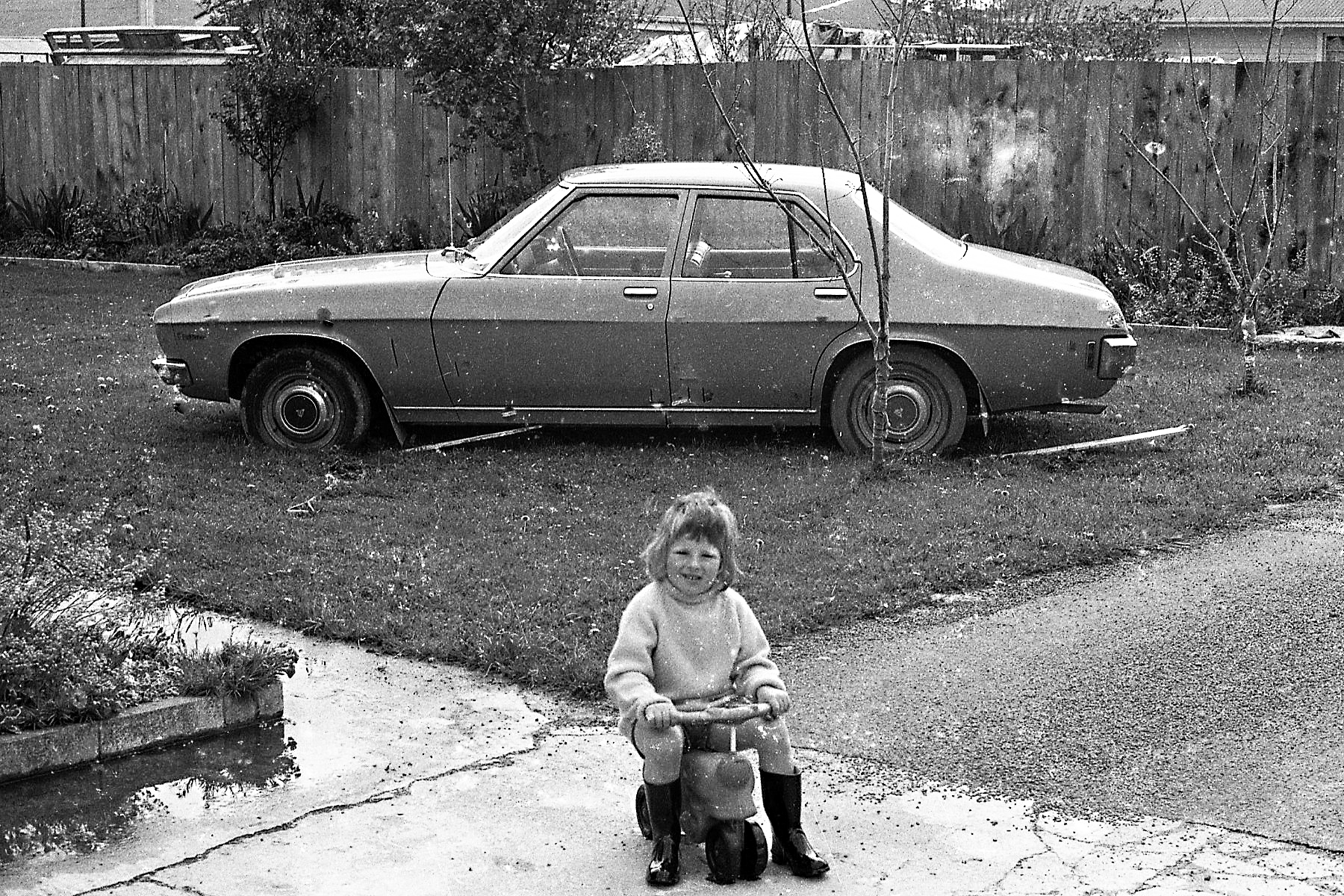 a girl sitting next to her old car in a driveway