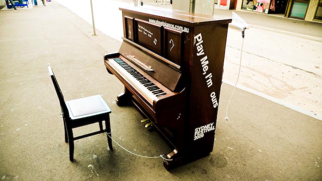 an upright piano and a chair stand on a sidewalk