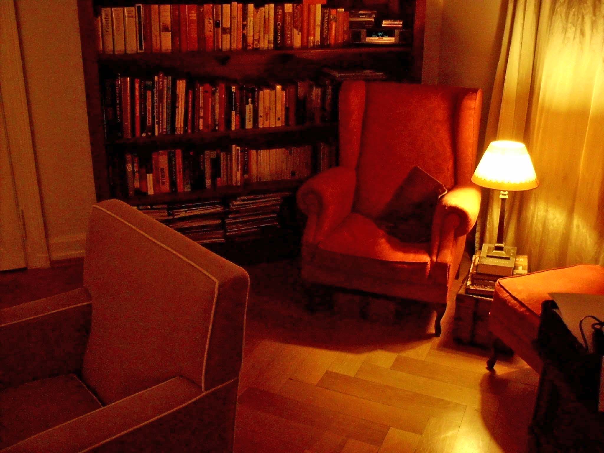 a chair sitting under a book shelf next to a lamp