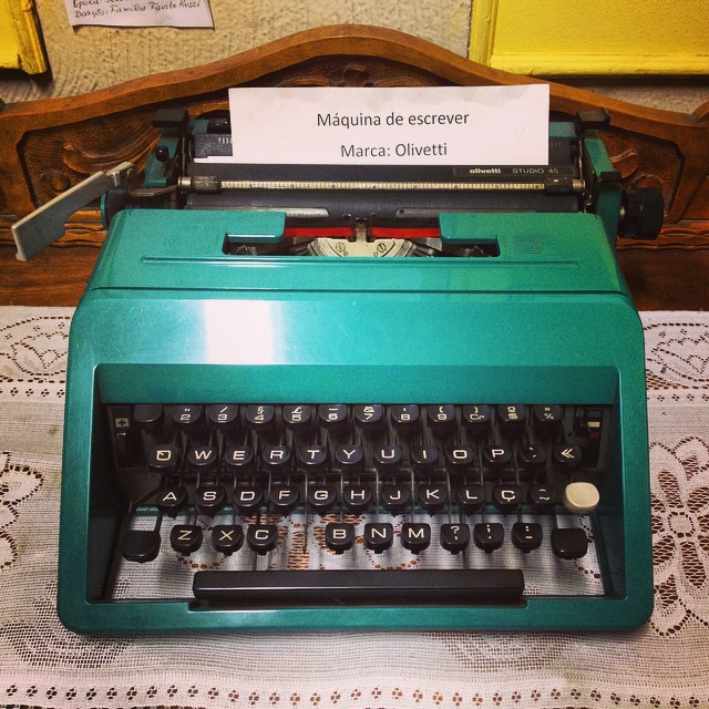 green typewriter with manual on table beside lace doilies