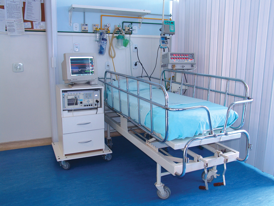 a hospital room with a bed, monitor and a drawer