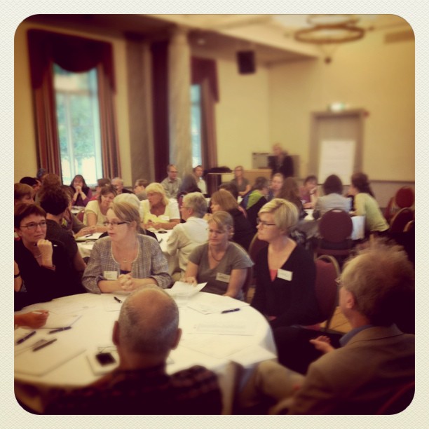 a group of people sitting around a table listening to a man speaking