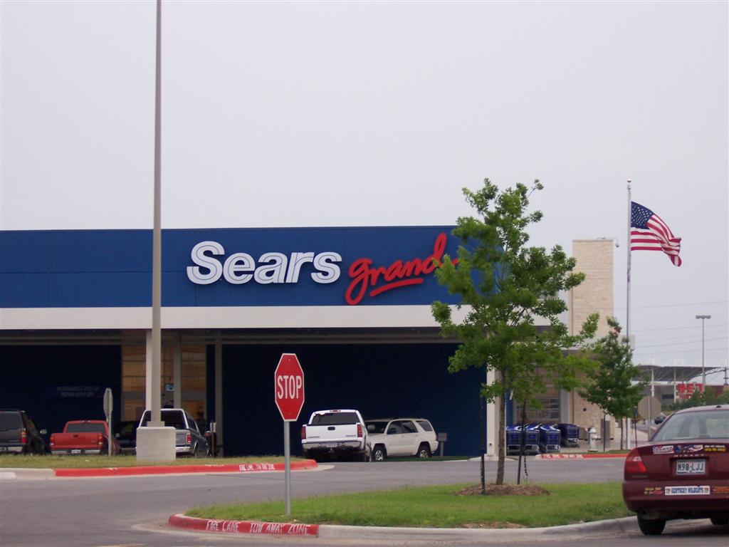 two cars are outside a sears's grand opening with american flag in background