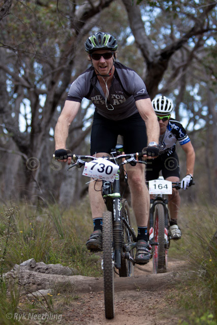 a man riding a bicycle down a dirt path next to a forest