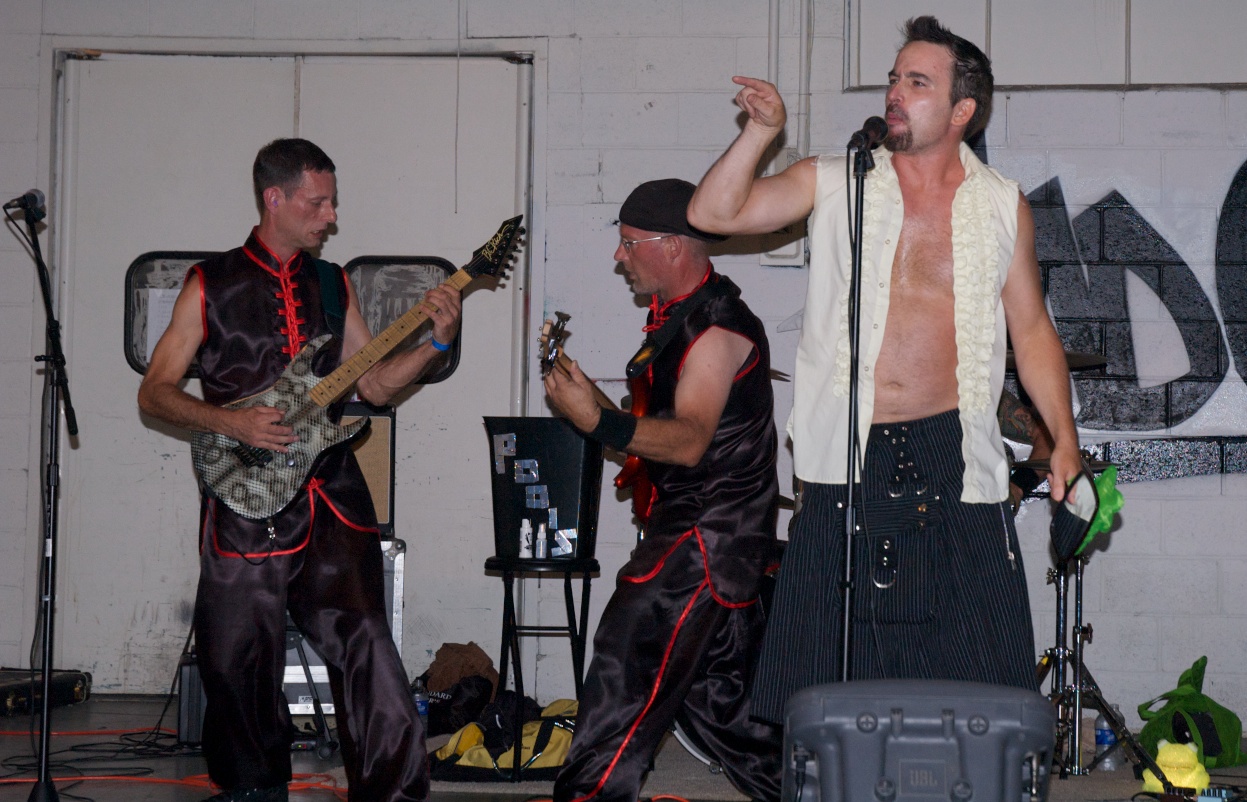 three shirtless men wearing black attire and holding guitars