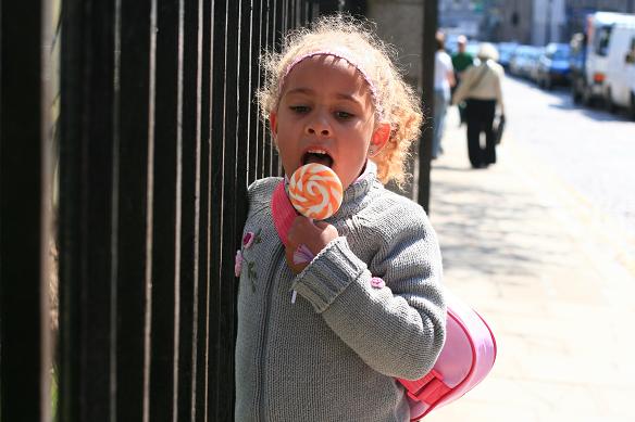 a little girl is looking at an orange lollipop