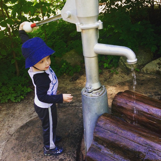 a little  with a blue cap looking at a water spout