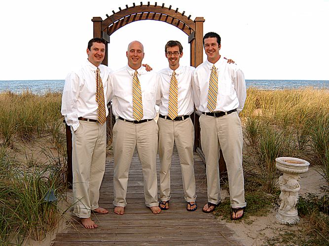 four men standing on the wooden walkway that leads to the beach