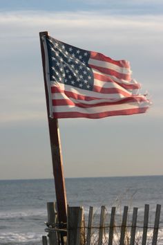 an american flag is flying from a wooden post near the ocean