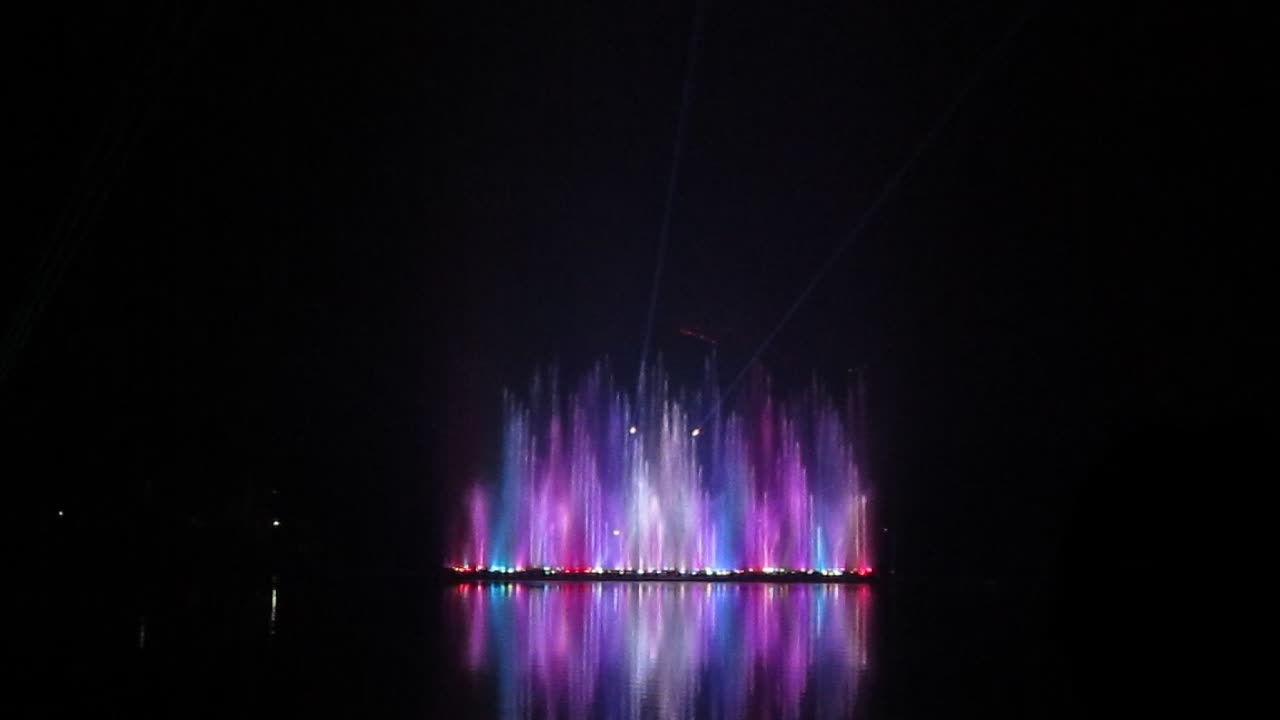 a brightly lit fountain in the dark with its reflection