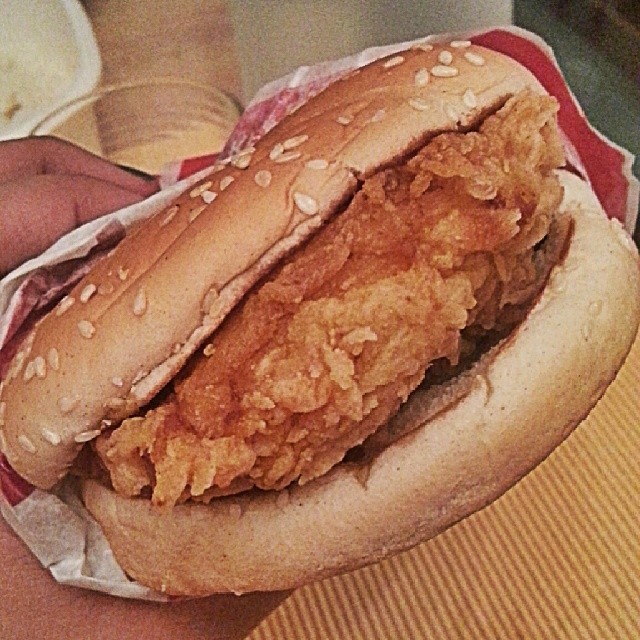 a person holding a sandwich with fried chicken on it