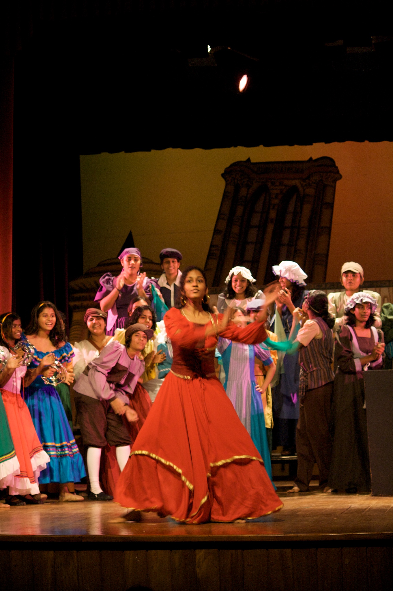 woman in orange dress performing on stage with a large group behind