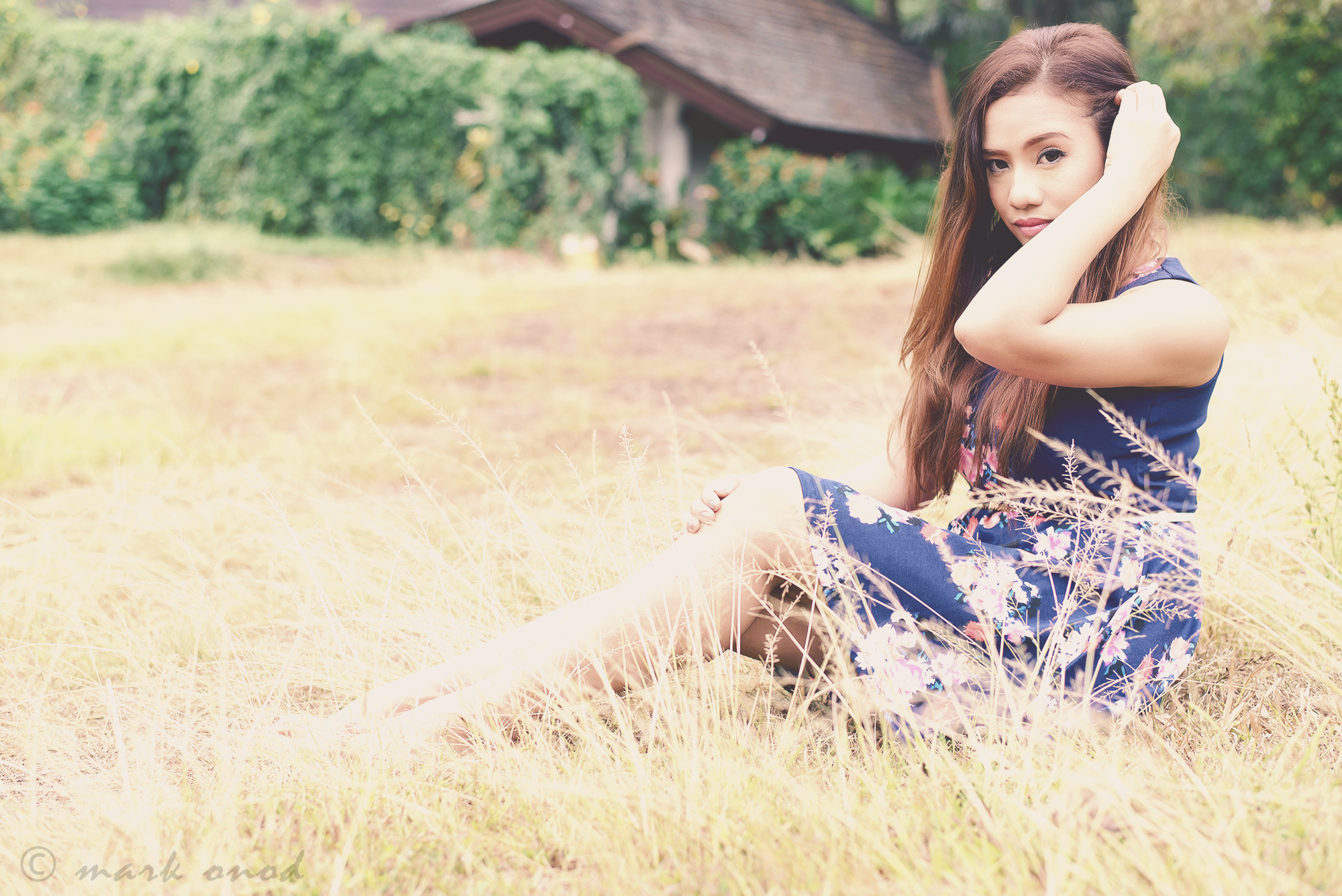 a woman sitting in a field near trees