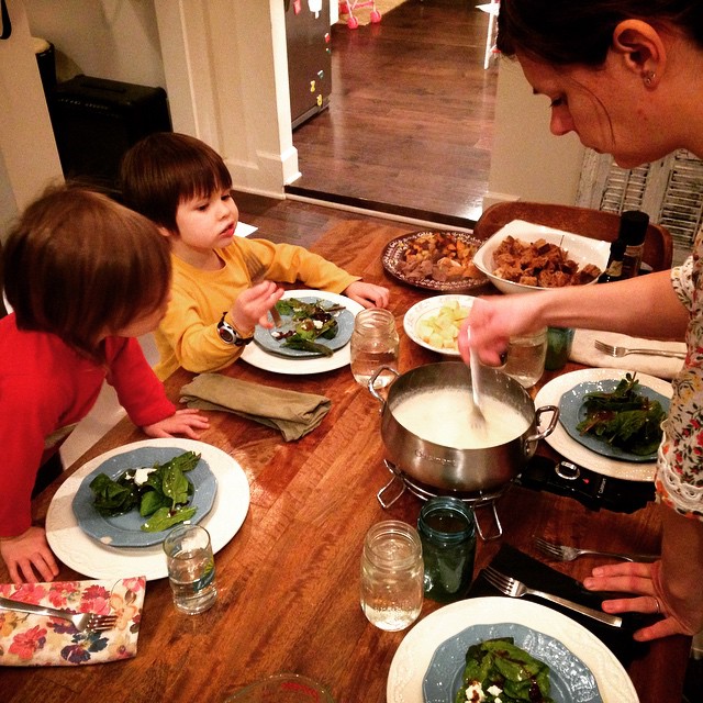 a  standing in front of two older children sitting at a table with food