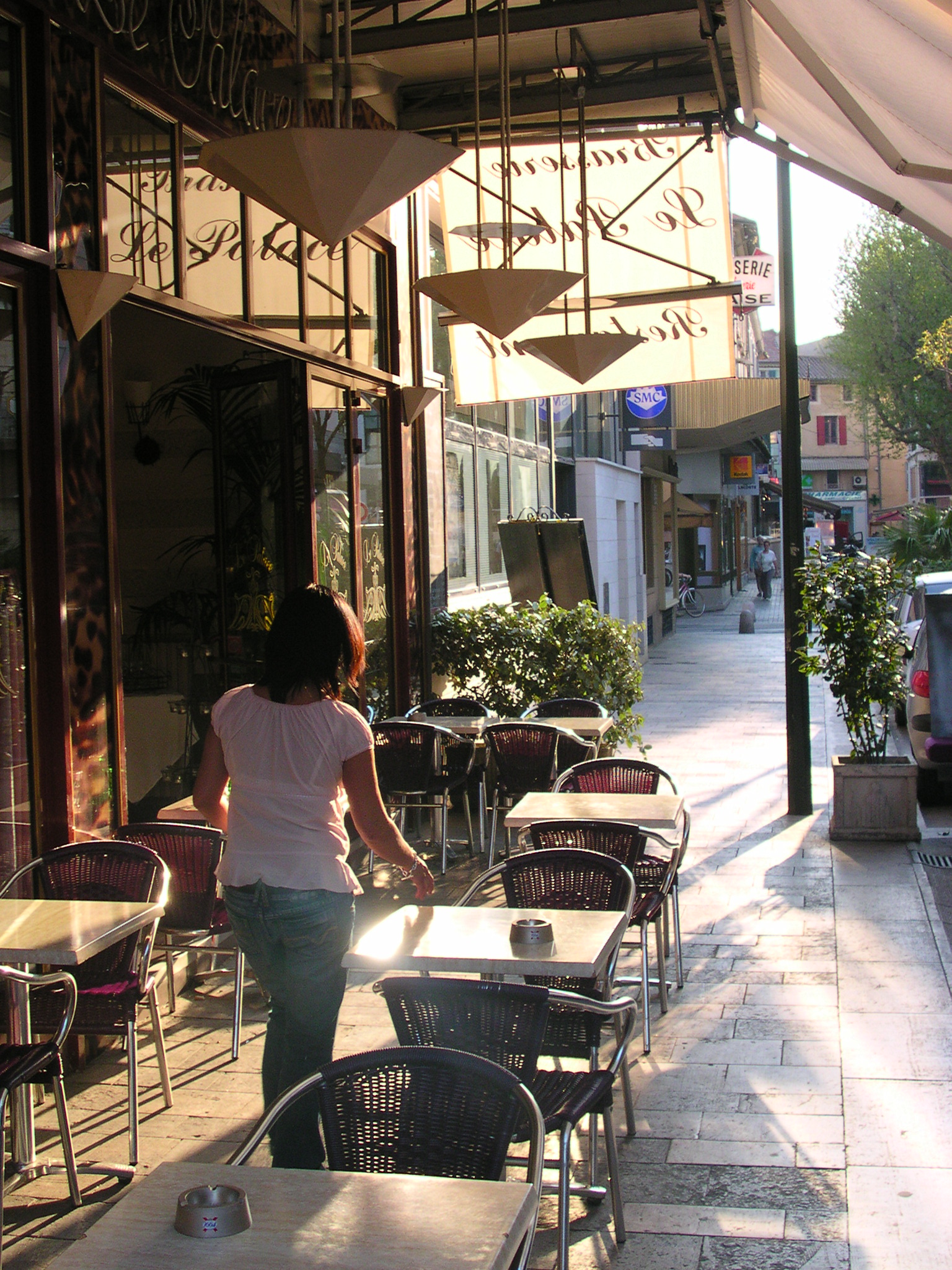 woman walking in front of a restaurant that has tables and chairs on it