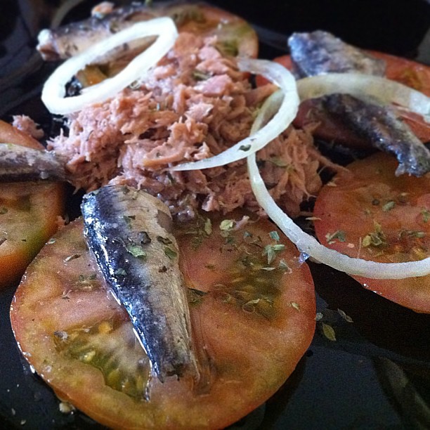 a plate filled with fish and tomatoes on top of a table