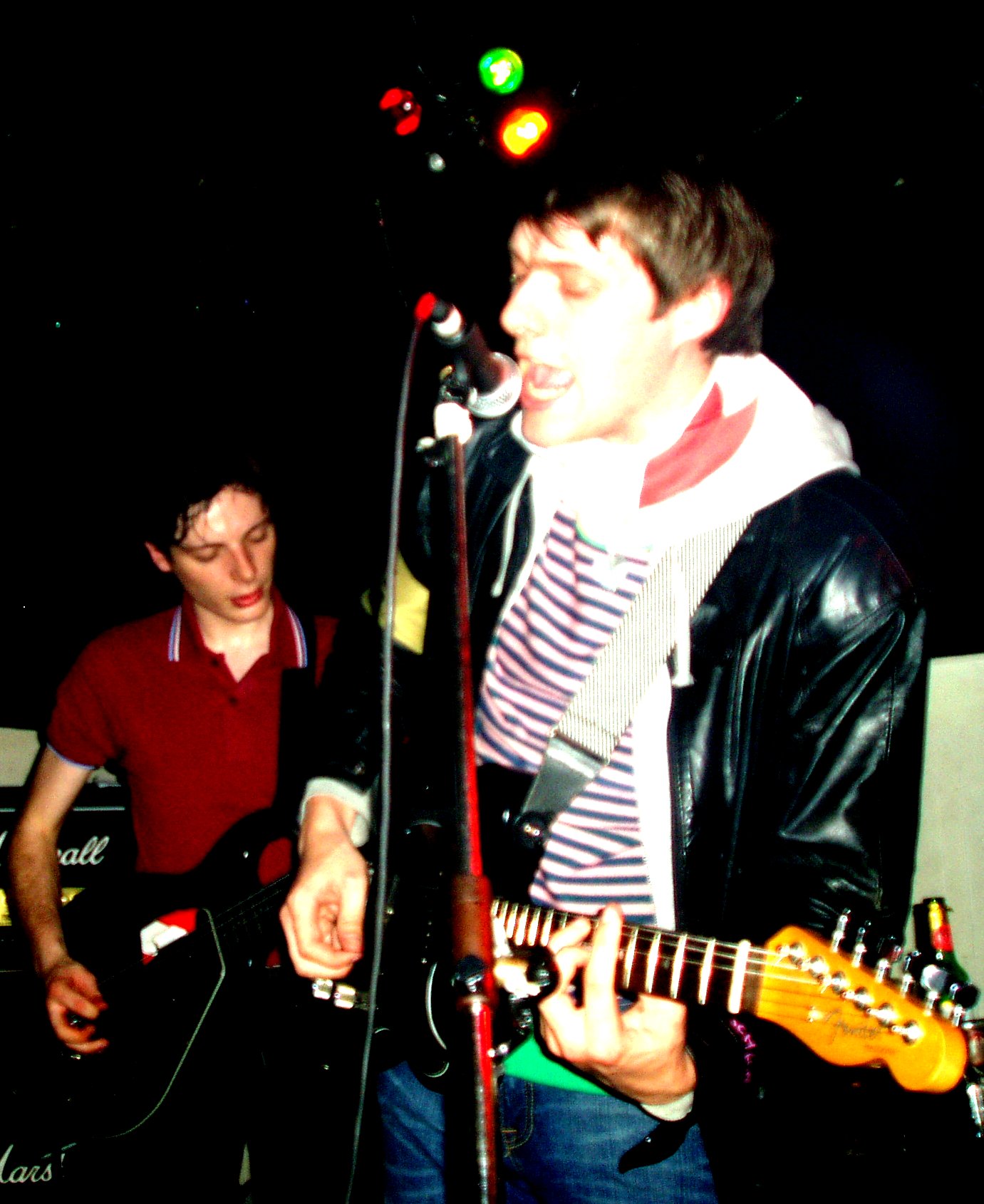 a male in a red shirt is singing and an on the same guitar player