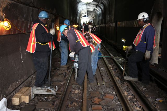 several workers working on railroad tracks at the bottom of a tunnel