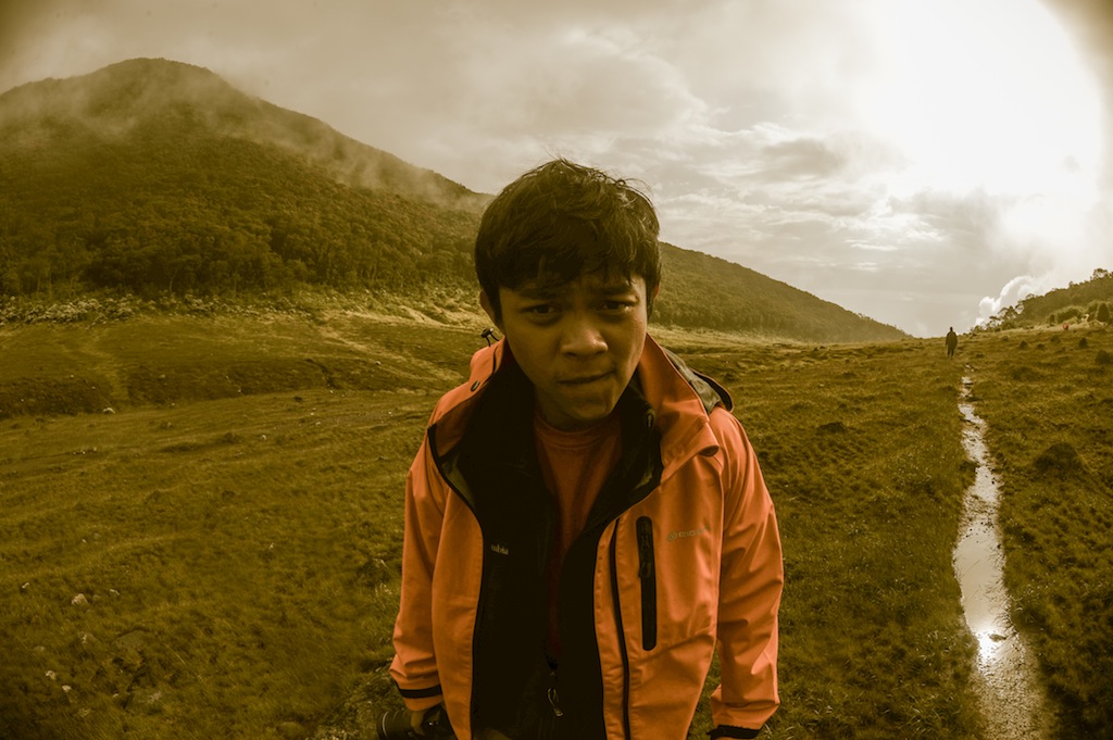 a boy standing in a field on the edge of the hill