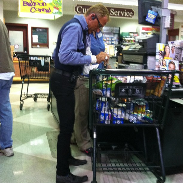 an elderly man in blue shirt standing next to a shopping cart