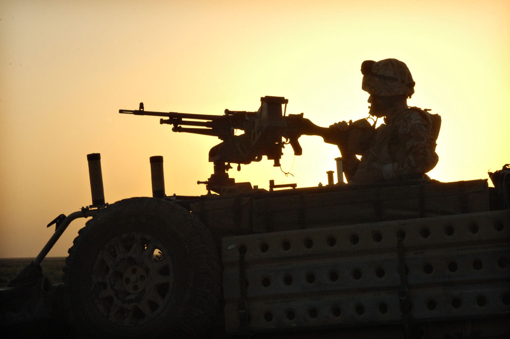 two men on an army vehicle, one holding a machine gun