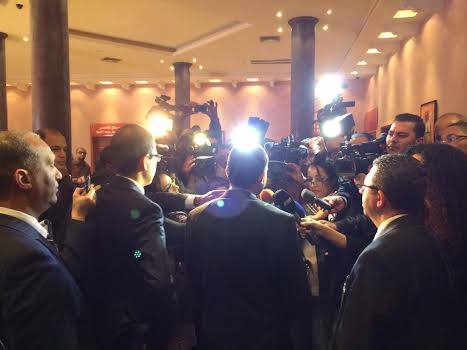 a crowd of reporters in suits are standing and talking