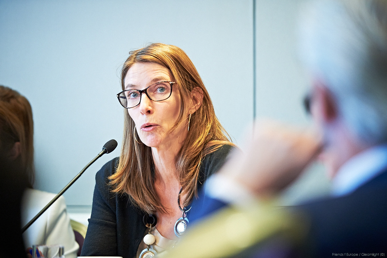 a woman in glasses and a jacket sitting at a table