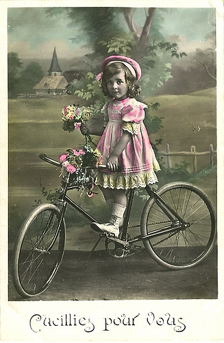 an old fashioned girl standing on a bicycle with flowers