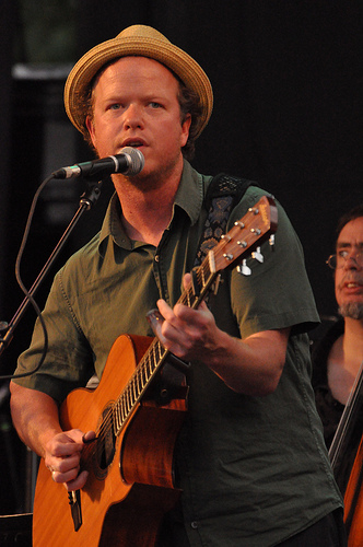 a man in a hat singing and holding a guitar