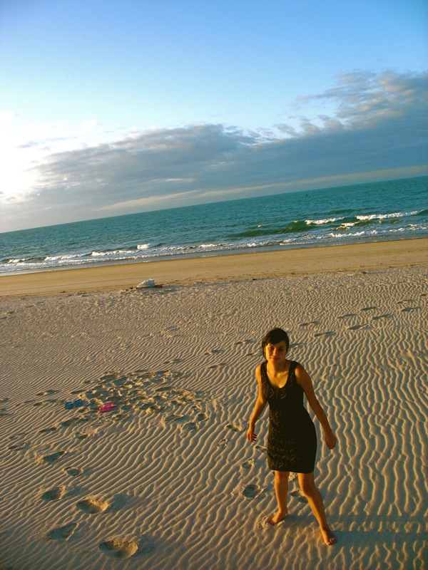 a woman in dress standing on a beach near water
