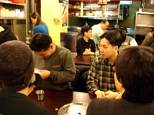 a man standing in a diner with another person looking at his cell phone