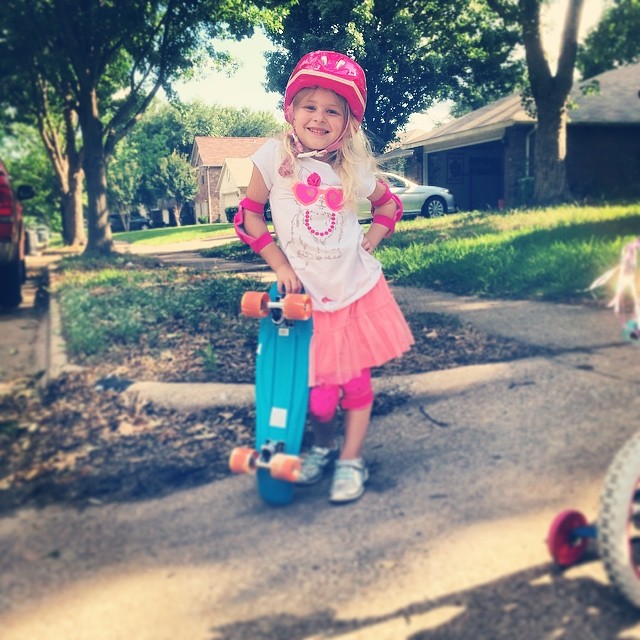 little girl on a skateboard standing on the sidewalk