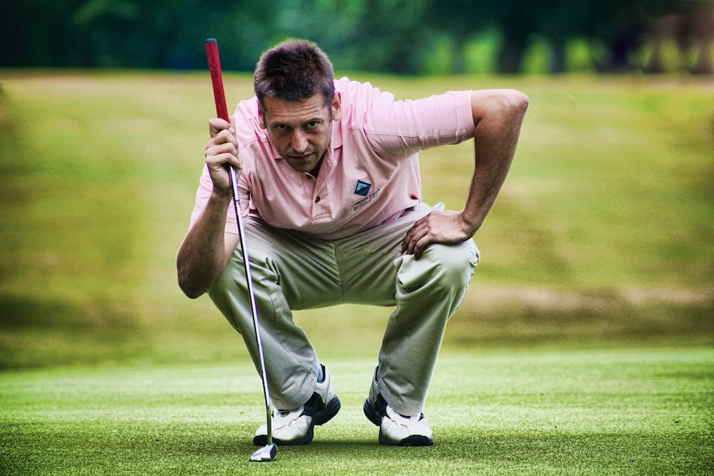 a man squatting down while holding his golf club and ball