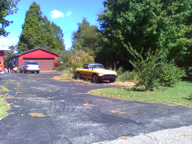 old, yellow, and black car sitting in front of a garage