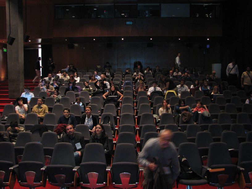 a room full of people sitting and standing in front of the speakers