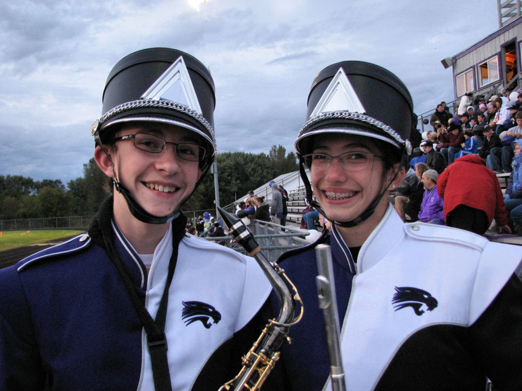 two girls in marching uniforms with instruments stand on a baseball field