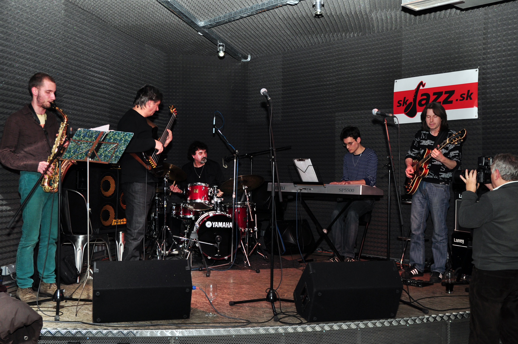 four men and two women playing musical instruments on stage