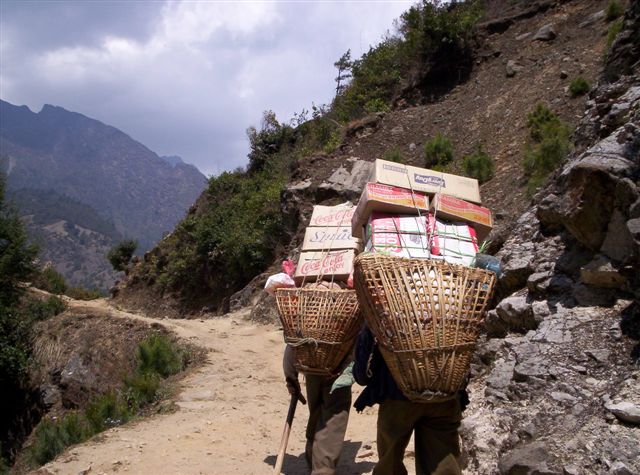 two people walking on the path with luggage strapped on to their backs