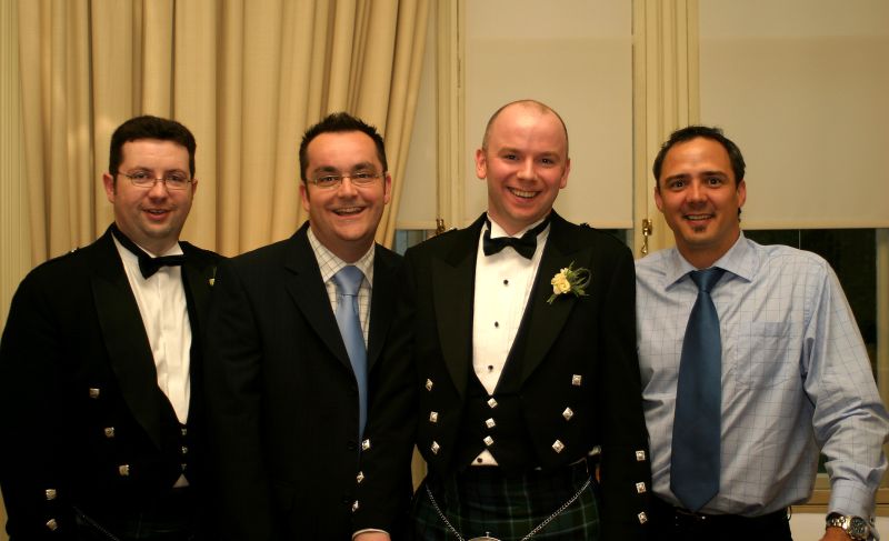 four men in black and white dresses smile at the camera